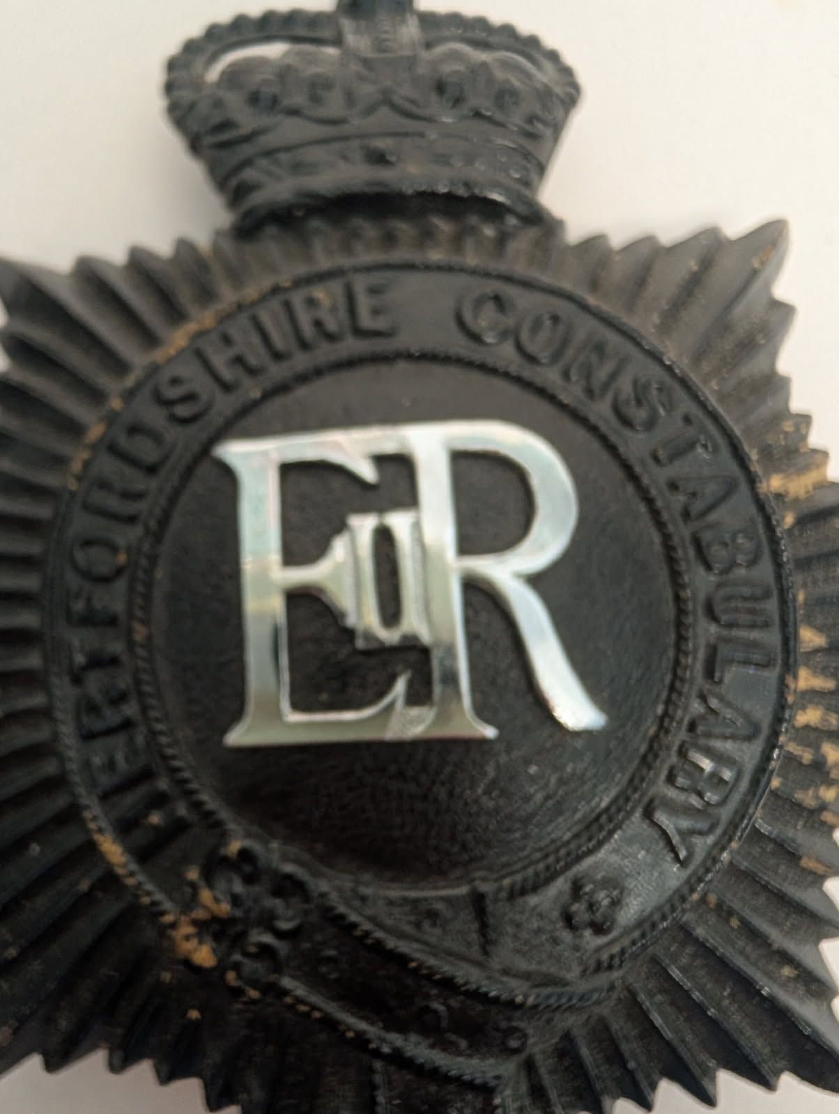 Black police badge with 'ER' initials and crown emblem on a white background