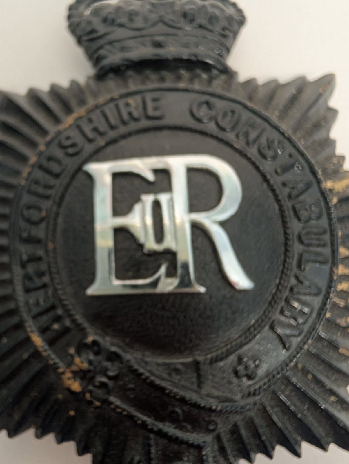 Black police badge with 'ER' emblem and crown on a white background